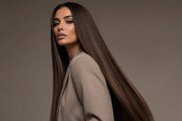 Naklejka premium A young woman with long dark hair wearing a beige blazer is posing against a plain brown background.