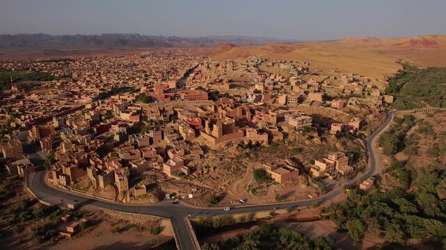 Tinghir in Draa-Tafilalet, Morocco, between the High Atlas and Jbel Saghro ranges, showing fortified mudbrick ksar architecture, curved transport corridors and expanding desert urbanization, parallax