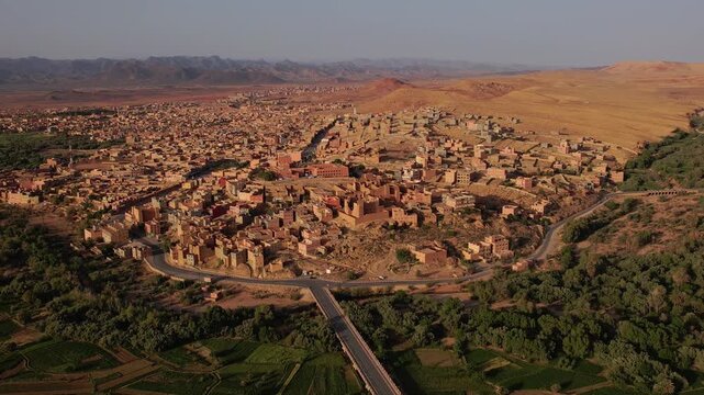 Tinghir in Draa-Tafilalet, Morocco, between the High Atlas and Jbel Saghro ranges, showing fortified mudbrick ksar districts, irrigated agricultural land and arid desert terrain, pullback orbit