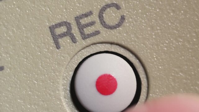 Angled macro shot of finger pressing white record button with red dot on beige controller