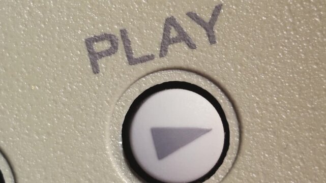 Angled macro shot of finger pressing white play button on beige editing controller