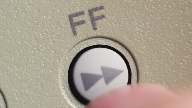 Angled macro shot of finger pressing white fast forward button on beige editing controller