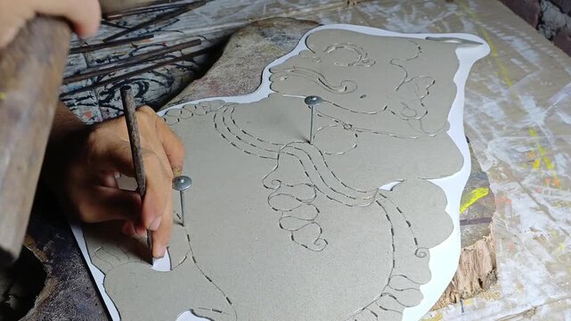 Close-up view of a traditional Indonesian craftsman carving and shaping a leather puppet for wayang kulit. The handmade artwork represents the rich cultural heritage of Java, showcasing intricate craf