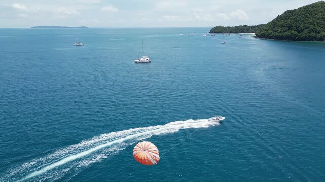 Aerial tracks parasailing person from high angle near tropical island