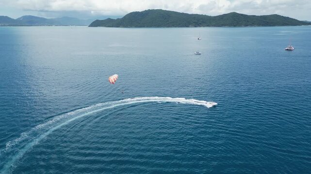 Aerial follows tourist parasailing behind boat in blue ocean, tourism