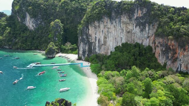 Flyover narrow tropical beach beneath tall limestone cliffs, tourism