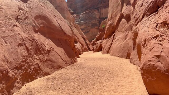 A wide-angle, eye level shot capturing the sandy floor and towering red sandstone rock formations in a slot canyon found within Antelope Canyon, Arizona.