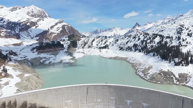Aerial Pullback Curved Hydroelectric Dam Amid Snow-Covered Mountains