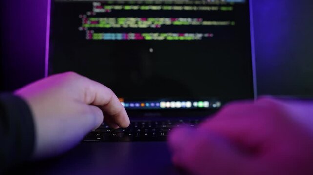 Dark cinematic close-up footage of a person coding on a laptop in a modern neon-lit environment with blue and purple ambient lighting.