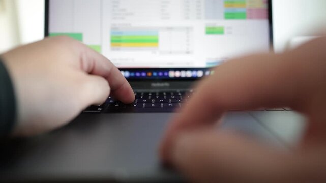 Close-up view of a laptop displaying a business analytics dashboard with statistics, pie charts, and performance data. Hands type on the keyboard while using the mouse to click and scrolling.