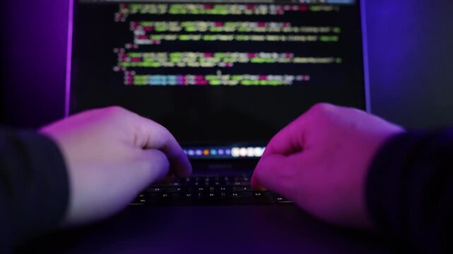 Dark cinematic close-up footage of software developer coding on a laptop in a modern neon-lit environment with blue and purple ambient lighting.