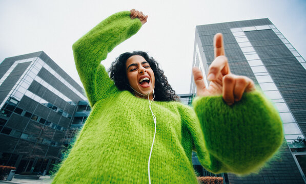 Woman dancing energetically in city with headphones and joy