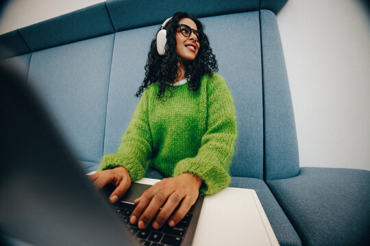 Headphones on, the woman works with a laptop in a relaxed indoor lounge