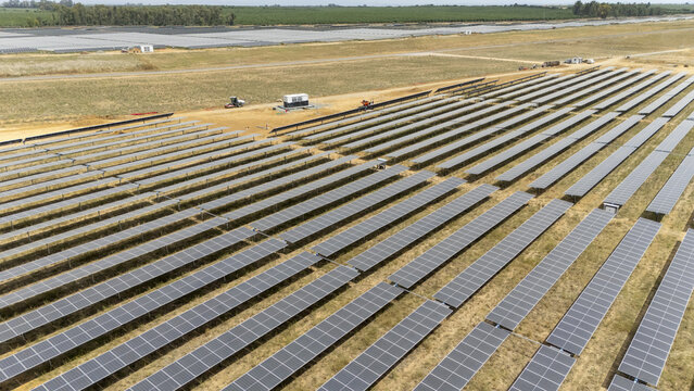 Aerial view of rows of solar panels in a large photovoltaic farm under construction with machinery in a dry rural landscape in Coria del Rio, Andalusia, Spain.