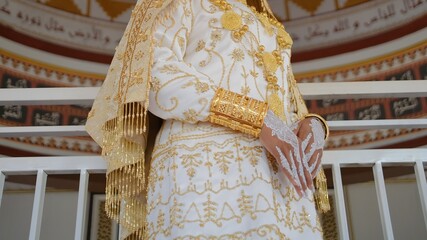 Side view of Indonesian bride wearing traditional Lampung attire with luxury golden jewelry against a mosque dome background.  © Agung