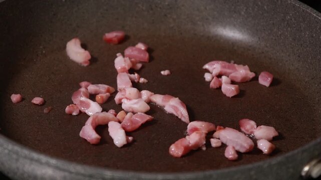 Close-up of savory bacon cubes sizzling and browning in a hot frying pan