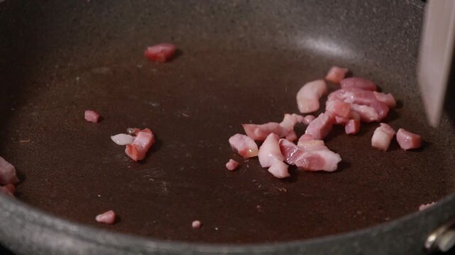 Close-up of savory bacon cubes sizzling and browning in a hot frying pan