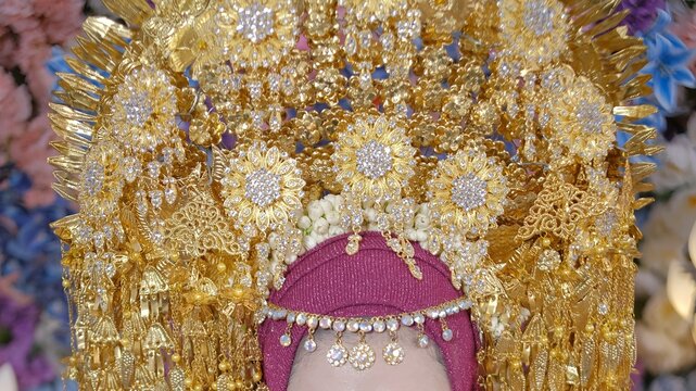 Beautiful Indonesian bride wearing majestic golden Siger crown against a colorful floral backdrop.