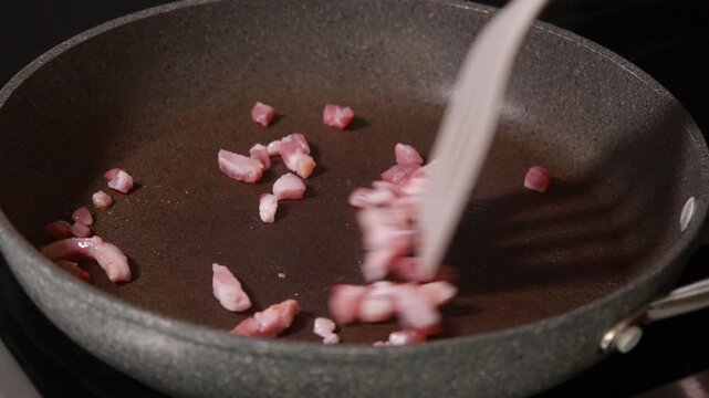 Close-up of savory bacon cubes sizzling and browning in a hot frying pan