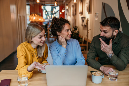 Coworkers collaborating on laptop discussing business project in cafe