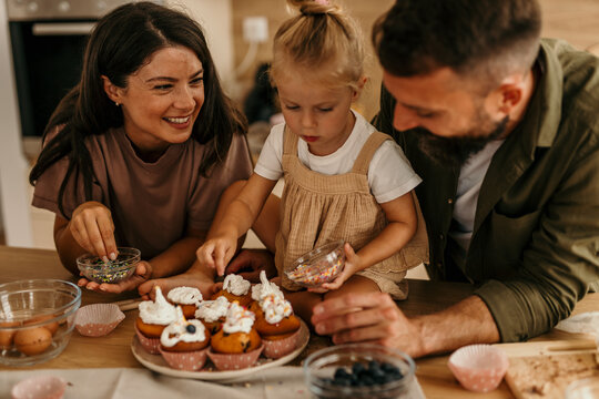 Family baking cupcakes with sprinkles in modern kitchen