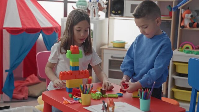 Girl and boy stack colorful plastic blocks with hands at a red table inside a building playroom; concentration cooperation play.