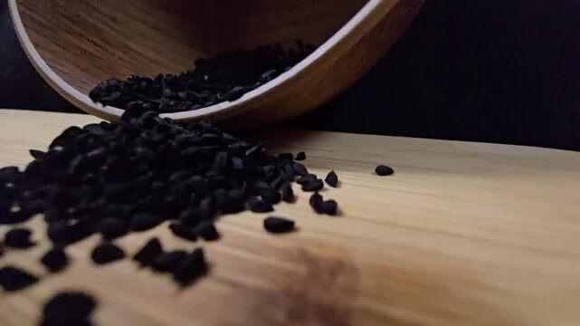 Macro shot of black seed, also known as nigella sativa or kalonji, spilling from a wooden bowl, perfect for herbal medicine and healthy food concepts.