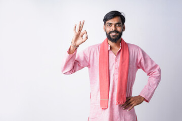 Fototapeta premium A smiling bearded man in a pink kurta and scarf stands against a plain studio background