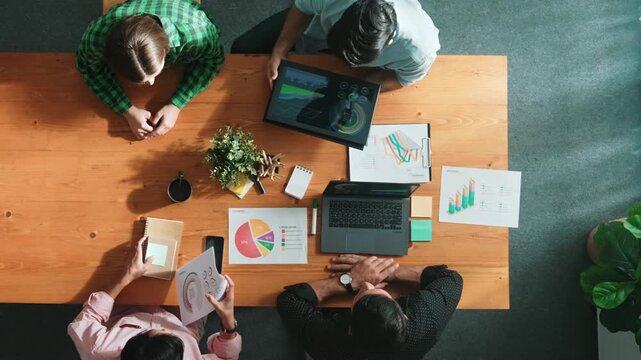 Top view of diverse business people working together to analyze chart. Top down aerial view of creative team looking at stock market report and discussing about financial investment. Convocation.