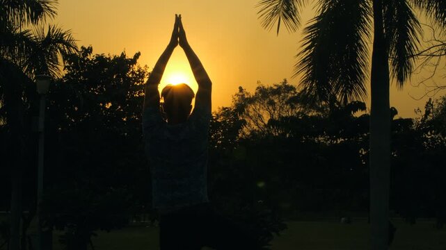 Rear view of a young male doing Surya Namaskar in a silhouette background. Indian youngster standing in Namaste posture/folded hands in front of the sun - meditation and Yoga concept