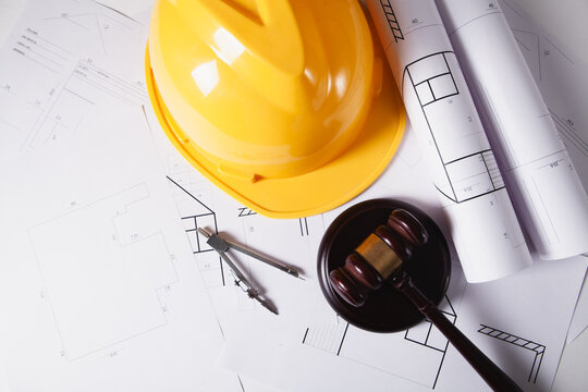 Wooden judge gavel, blueprints and hard hat on table