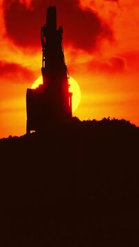 Excavator silhouette working during a fiery red sunset
