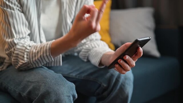 A person is seated on a couch, engaged with a smartphone and showing different hand gestures.