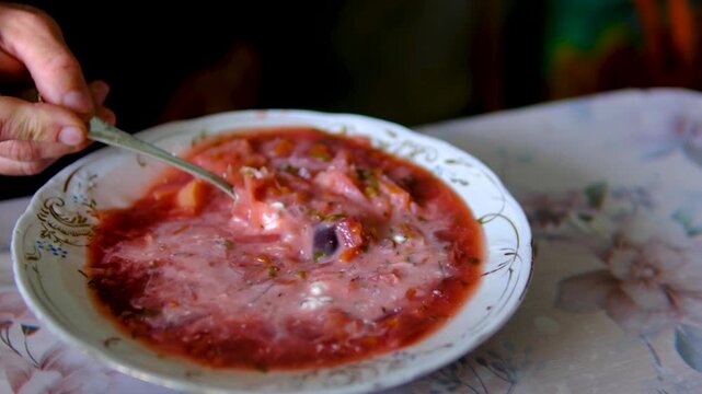 man enjoys traditional homemade borscht with sour cream, garlic lard. Cozy kitchen atmosphere, hearty lunch or dinner and authentic comfort food. mix delicious borscht with sour cream a tablespoon.