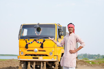 Smiling Indian truck driver posing proudly beside a yellow dumper truck on a rural roadside © Niks Ads