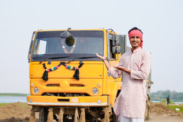 Smiling Indian truck driver posing proudly beside a yellow dumper truck on a rural roadside © Niks Ads