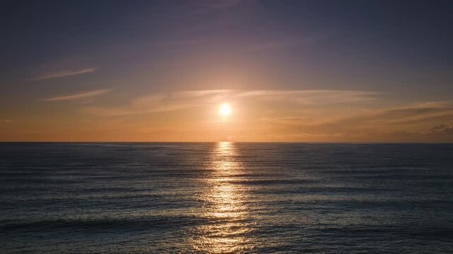 Static landscape timelapse capturing a dramatic golden sunset over the sea, transitioning into a vibrant afterglow with orange, pink, and deep blue twilight sky as night falls over the undulating