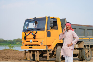 Young Indian truck driver in traditional attire talking on mobile phone beside a yellow dumper truck © Niks Ads