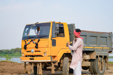 Young Indian truck driver in traditional attire talking on mobile phone beside a yellow dumper truck © Niks Ads