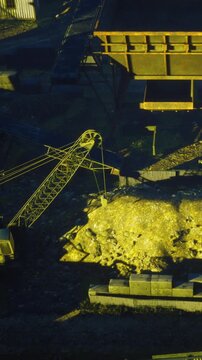 Heavy machinery operates on a construction site. Metal containers are lined up in organized rows. The scene is lit by the warm light of sunset in a mining area.