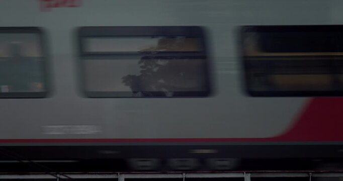 A passenger train rushes past in a blur of motion, its windows and red-striped body streaking across the frame at high speed.