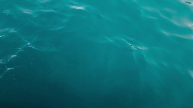 Smooth teal sea water surface with gentle ripples and soft light reflections, 4K video footage from boat. Perfect minimal ocean background or overlay.