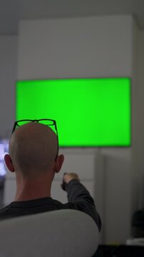 Man watching tv with green screen at home