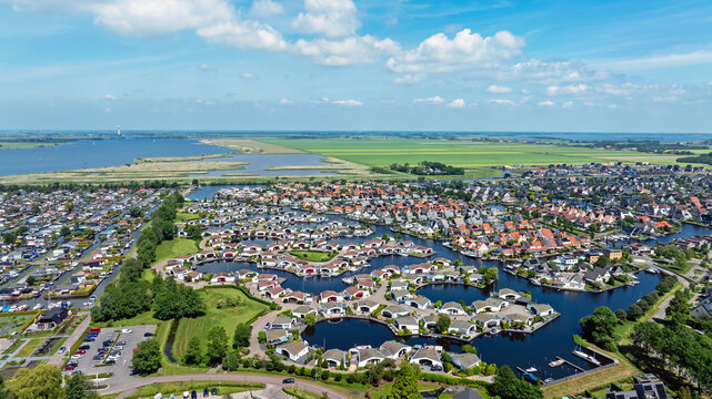 Aerial view of modern waterfront houses and boat docks along winding canals under a blue sky with white clouds in Lemmer, Friesland, Netherlands.