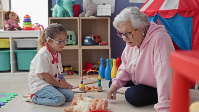 Woman kneeling with girl roleplaying doctor, holding a toy stethoscope and examining a baby doll in a daycare playroom; intergenerational bonding tenderness.