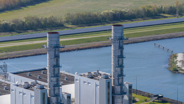 Aerial view of the Engie Maxima power plant featuring two tall industrial chimneys and solar panels along a waterway in Lelystad, Flevoland, Netherlands.