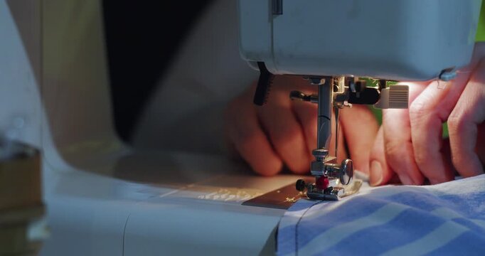 A close-up video shows hands sewing blue fabric on a machine, guiding it with care and precision. The rhythmic motion of the needle creates clean, even stitches. 60 fps 4k footage.