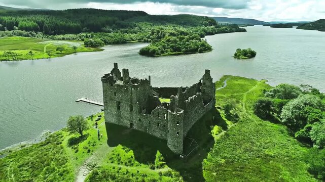 Cinematic aerial drone footage slowly orbiting a remote abandoned Scottish castle surrounded by rugged Highland scenery. The camera gracefully pans around the weathered stone ruins, revealing dramatic