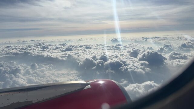 Sunlight streams through fluffy clouds as seen from an airplane window, creating a serene and expansive sky view. Ideal for travel and aviation themes.