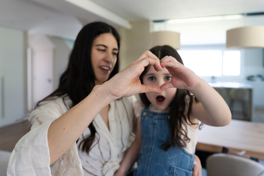 Mother and daughter making a heart shape with hands at home